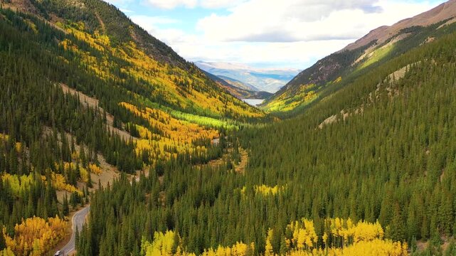 The Uinta Mountains in Utah glow in autumn light as winding roads climb toward rocky peaks surrounded by endless forests of yellow and green.