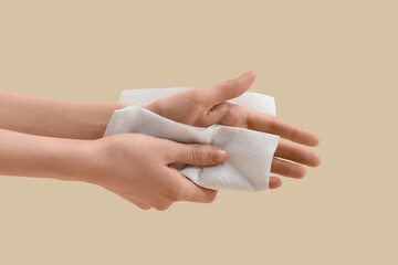 Young woman wiping hand with paper napkin on beige background, closeup