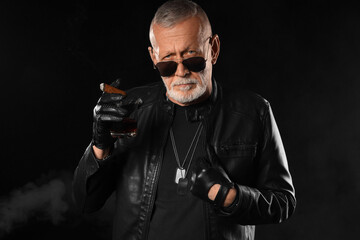 Stylish old man in leather jacket with cigar on black background