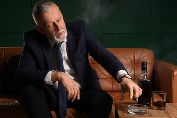 Old businessman putting out his cigar in ashtray at home