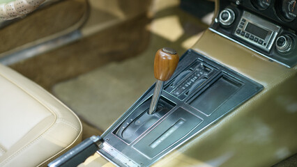 Vintage car interior featuring wooden gear shift, tan leather upholstery, and analog dashboard controls that showcase mid-century automotive design and craftsmanship.