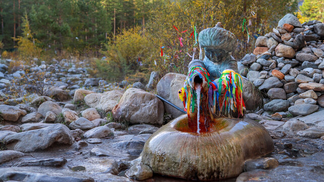 A close-up of a spring of healthy drinking mineral water in the form of a sculpture of a Buryat boy with colorful ribbons. Arshan, Buryatia, Kyngyrga River.