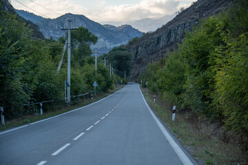 Straight empty highway between forest hills with dramatic sky