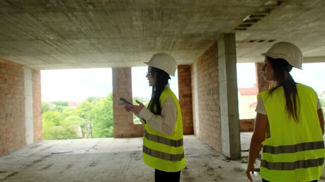 Female engineers inspect work areas during verification process. Ladies in hard hats and vests analyze results of tasks assessing project stage