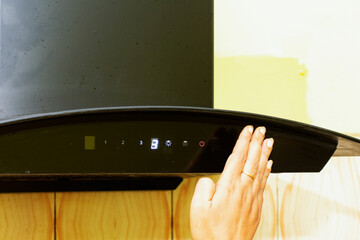 Woman operating modern kitchen chimney by waving hand in front of motion sensor