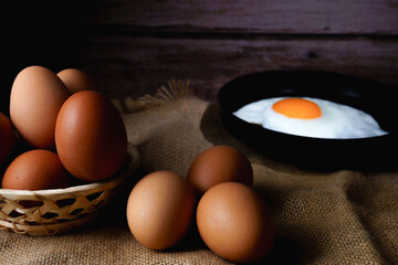 Fresh brown eggs in a basket and fried egg in a pan on burlap fabric