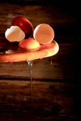Broken egg and yolk dripping from a rustic wooden spoon on a dark background
