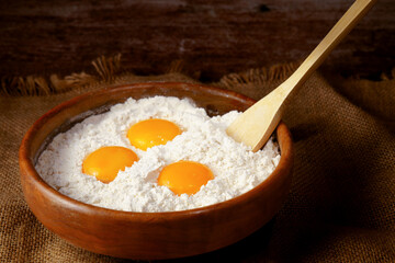 Flour, egg yolks, and a wooden spoon in a bowl, preparing ingredients for baking