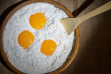 Bowl with flour, three raw egg yolks, and a wooden spoon, ready for baking