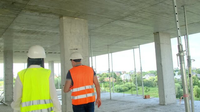 Worker and female engineer perform walkaround of building. Builder and manager inspect work areas evaluating results of project implementation