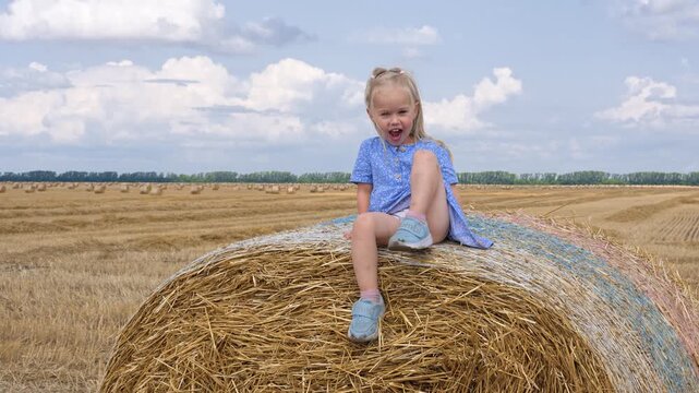 Cute little child sits on a haystack in a rural field in summer