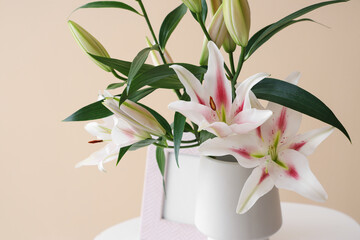 Vase with beautiful lily flowers on coffee table near beige wall, closeup