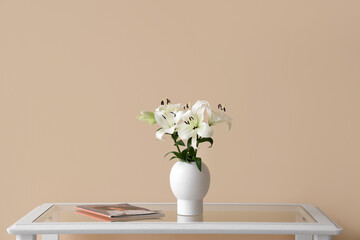 Vase with beautiful lily flowers and magazine on glass coffee table near beige wall