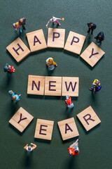 Miniature figurines surrounding wooden letter tiles forming the phrase Happy New Year