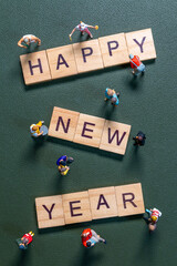 Miniature figurines surrounding wooden letter tiles forming the phrase Happy New Year