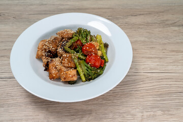 Stir-fried red snapper with teriyaki sauce and various vegetables: broccoli, tomatoes, asparagus, and baby corn on wooden table.
