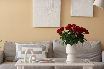 Vase with beautiful red roses on glass coffee table in stylish living room