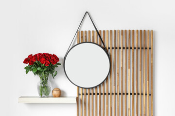 Vase with beautiful red roses and aroma oil diffuser on shelf in stylish room