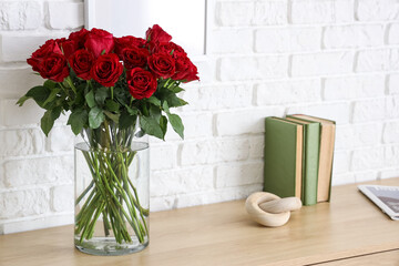 Vase with beautiful red roses, books and decor on wooden cabinet in stylish room