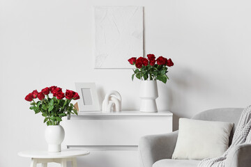 Vases with beautiful red roses on coffee table and chest of drawers in stylish living room