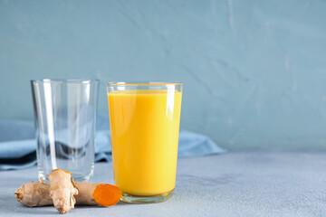 Glass of healthy turmeric drink and ginger roots on blue grunge background, closeup