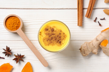 Glass of healthy turmeric drink and ingredients on white wooden background, closeup