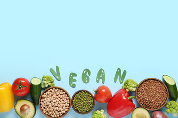 Different fresh vegetables, buckwheat and legumes with word VEGAN on blue background