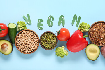 Different fresh vegetables, buckwheat and legumes with word VEGAN on blue background