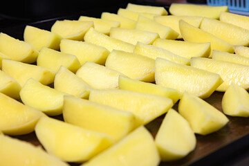 Freshly cut yellow potatoes ready for roasting at a kitchen prep station in the afternoon sun, lined up for cooking