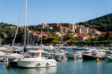 A Long Row of White Yachts and Sailboats Moored in the Harbor with Tall Masts Against a Hillside of Houses and a Deep Blue Sky in Lerici, Italy