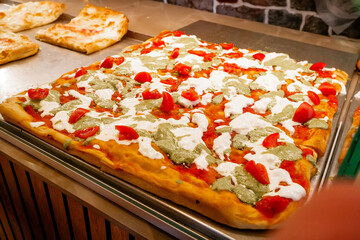Close-up of Traditional Italian Pizza al Taglio Topped with Cherry Tomatoes, Mozzarella, and Green...