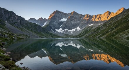 Serene mountain lake reflecting the golden hues of dawn, framed by towering, snow-capped peaks.