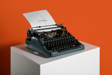 Vintage typewriter on pedestal against orange background