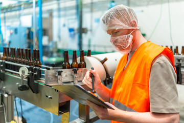 Worker inspecting beer bottling process in factory