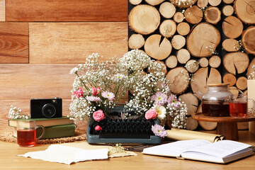 Vintage typewriter with flowers, tea and books on table near wooden wall