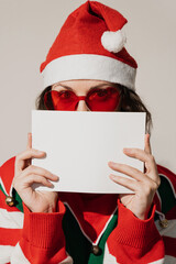 Woman in Santa hat and elf costume holding white card with sunglasses