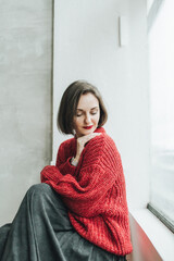 Woman wearing cozy red cable knit sweater in natural window lighting setting