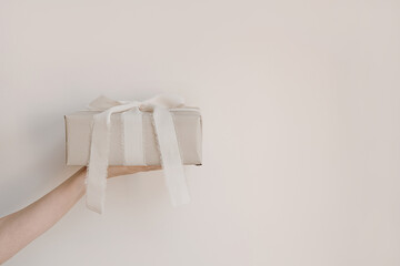 Gift box with beige ribbons in hand. Birthday gift with copy space for holiday. Christmas present