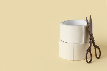 Rolls of white masking tape with scissors on beige background