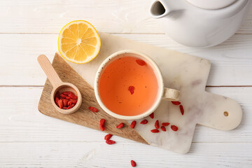 Cup of hot goji tea with lemon and berries on white wooden background