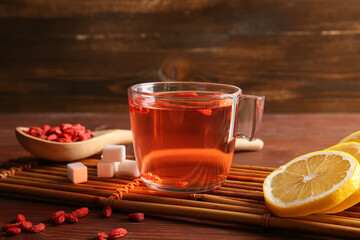 Glass cup of hot goji tea with lemon and cubes of sugar on wooden background