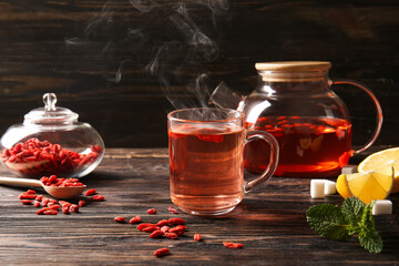 Glass cup of hot goji tea with mint and lemon on wooden background