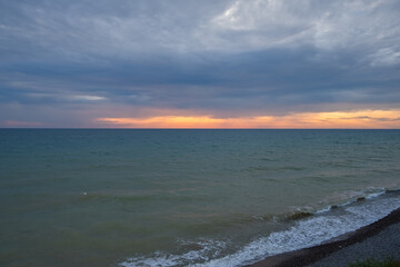 Orange sunset on the sea. Bright juicy landscape with feathery clouds on the horizon. Purple, lilac, pink shades of the evening sky. A calm turquoise sea rolls onto the beach. Idyll, relaxation