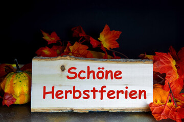 Holztafel mit der Aufschrift SCHÖNE HERBSTFERIEN und herbstliche Dekoration