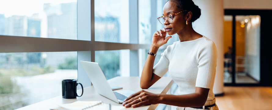 Fototapeta Woman using laptop and thinking while working near large window