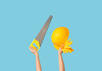 Hands with hardhat, gloves and handsaw on blue background