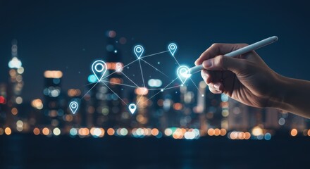Hand using stylus to connect digital location pins in a network over a blurred city skyline at night