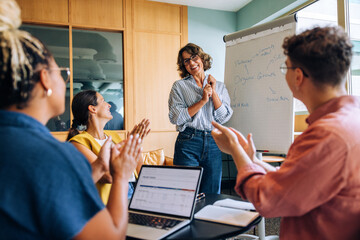 Team members applaud a woman leading a presentation in an office setting