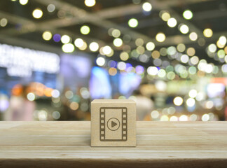 Play button with movie flat icon on wood block cube on wooden table over blur light and shadow of shopping mall, Business cinema online concept