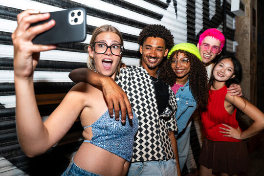 Multiethnic group of young friends having fun on the streets in the night - Stylish cool multiracial people wearing stylish clothing hanging out before party in a disco club - Powered by Adobe
